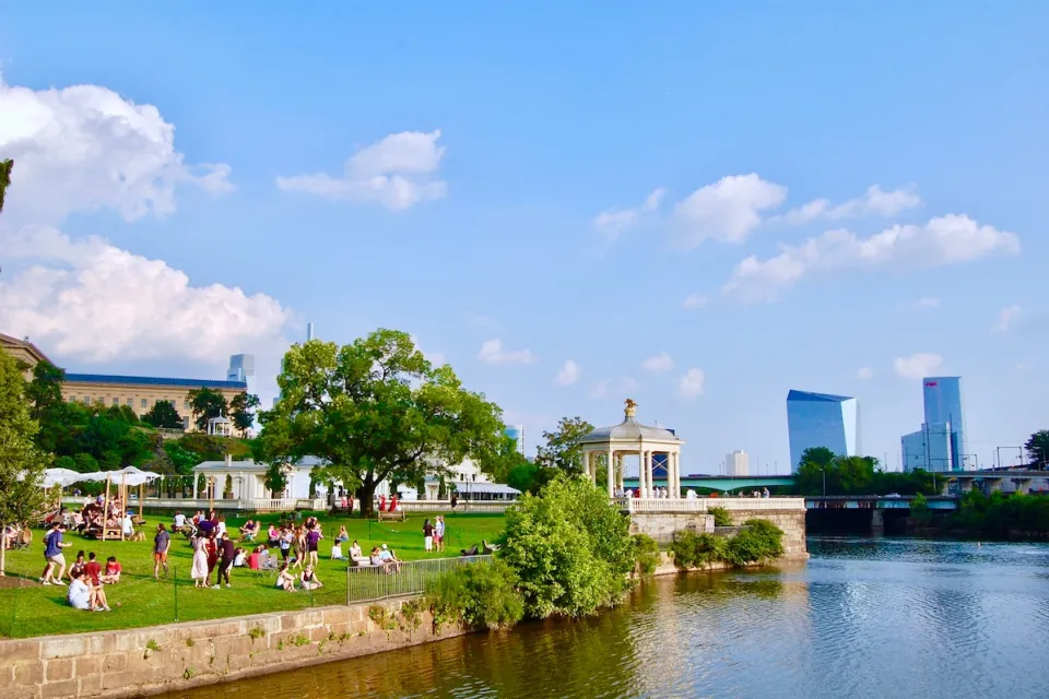Riverfront park in Philadelphia with white gazebo and skyscrapers in background.
